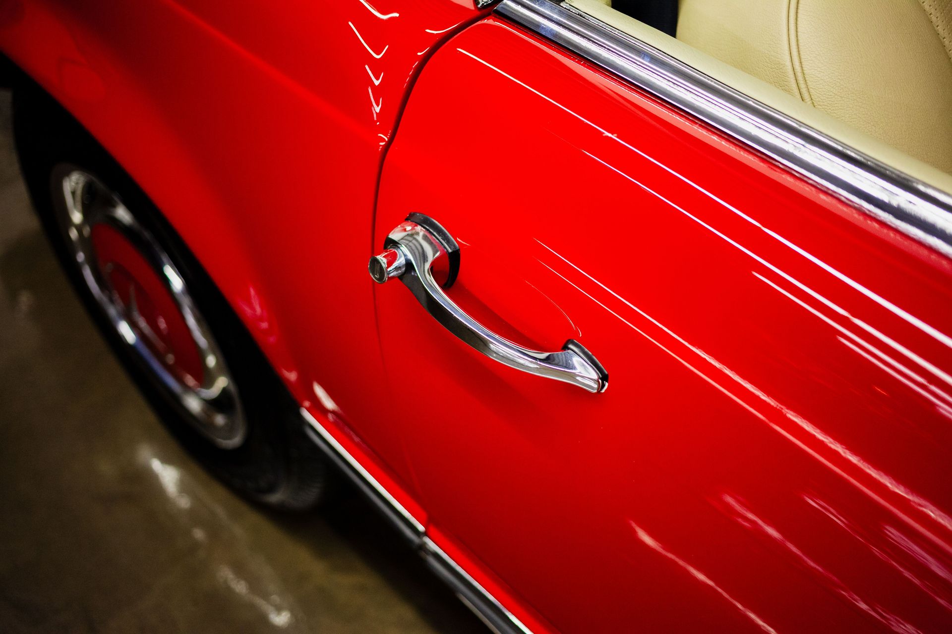 Detailed shot of a classic car's red door and chrome handle captured indoors.